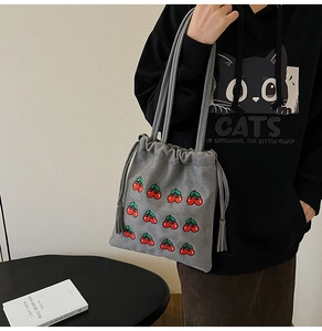 Detail of grey suede bucket bag featuring 12 embroidered cherry patterns and drawstrings