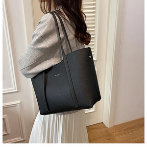 Detalle de bolso tote negro de cuero granulado con logo dorado en el hombro de la modelo