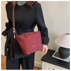 Detail of burgundy matte suede bucket bag with wide shoulder strap and silver hardware
