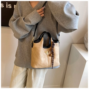 Détail d'un sac cabas beige vintage avec poignées noires et pendentif cloche tressé