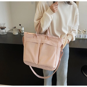 Pink large capacity nylon tote bag with front pockets worn by model in a cafe