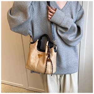 Détail d'un sac cabas en cuir mat beige avec bordure noire et breloque tissée décorative