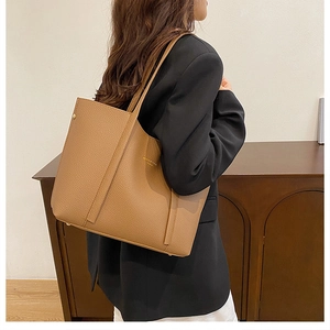 Bolso tote de cuero marrón con letras doradas mostrado al hombro en ambiente de oficina