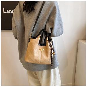 Détail du sac cabas beige avec bordures noires et emblème métallique triangulaire
