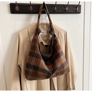 Detail of a brown plaid hobo bag with knotted shoulder strap hanging on a wooden hook