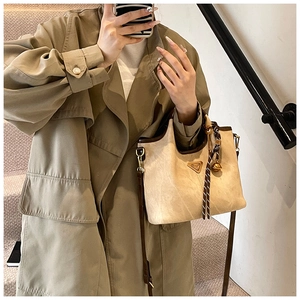 Détail du sac cabas beige avec bordure marron, logo triangle et breloque cloche