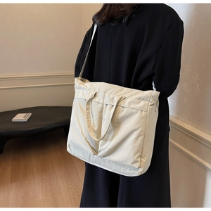 Lifestyle shot of model wearing a large cream nylon tote bag with dual shoulder straps