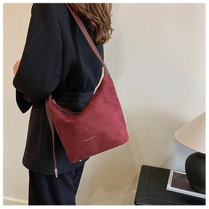 Side view of a burgundy suede hobo bag with slim leather straps and gold metal feet