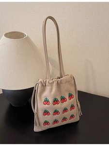 Minimalist beige suede bucket bag with red cherry embroidery and tassel drawstring detail