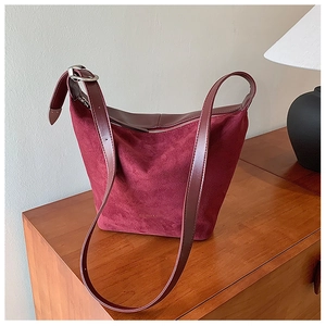Macro detail of wine red suede tote bag with leather trim on a vintage wooden cabinet