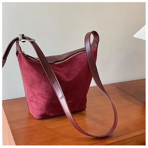 Detail of burgundy suede shoulder bag with smooth leather trim and metal buckle on wood