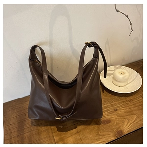 Detail of a large coffee leather hobo bag with adjustable gold buckle on a wooden table