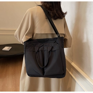 Model wearing a large black matte nylon tote bag with wide shoulder strap in daily setting