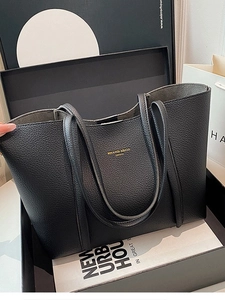 Bolso tote grande de cuero negro con logo dorado sobre fondo de caja de regalo