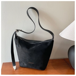 Detail of black matte suede bucket bag with adjustable strap on a wooden desk