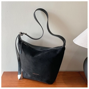 Detail of black suede tote bag with leather straps and 'FASHION & BAGS' logo on wood