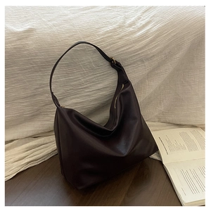 Detailed shot of dark leather hobo bag with vintage copper buckle on dark wood floor