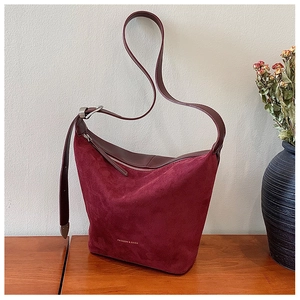 Detail of burgundy suede and leather hobo bag with adjustable strap on wooden surface