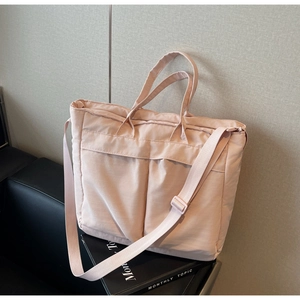Detail view of large nude pink nylon tote bag with two front pockets on a leather sofa