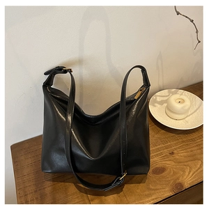Detail view of large black leather hobo bag with gold zipper on a wooden table