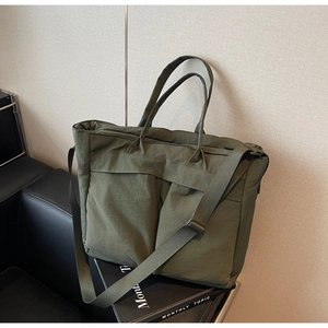 Detail of army green nylon tote bag featuring front pockets and adjustable strap on chair