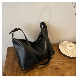 Detail of minimalist black leather crossbody bag on wood with gold zipper and strap