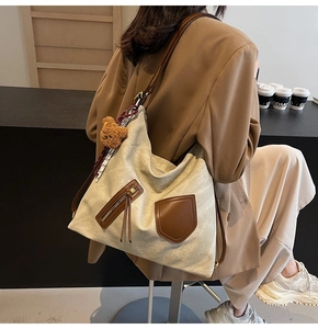 Detail of canvas tote with brown leather pockets and plush bear charm on model