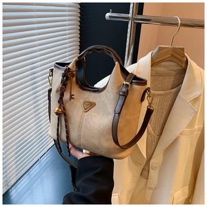 Détail du sac fourre-tout beige avec bordure marron foncé, logo en métal et pendentifs