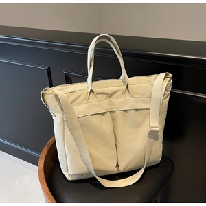 Detail of beige nylon tote bag with dual front pockets and adjustable wide strap