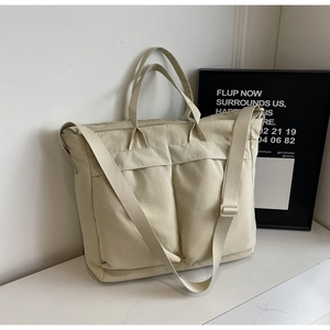 Detail view of cream white tote bag with dual front pockets and adjustable strap