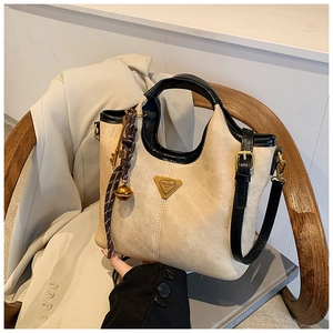 Gros plan détaillé du sac cabas beige avec plaque triangulaire dorée et breloques décoratives