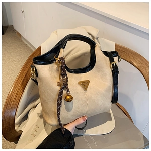 Détail du sac seau en daim avec logo triangulaire doré et breloque clé rétro sur chaise