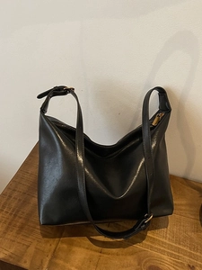 Large black faux leather hobo shoulder bag with gold zipper on wooden table
