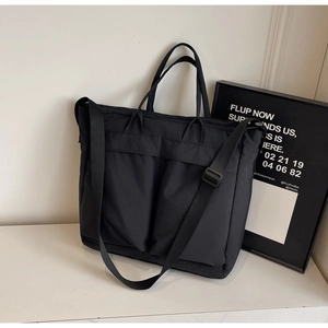 Detail view of black nylon tote bag with dual front pockets and adjustable shoulder strap