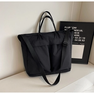 Detail view of large black tote bag with dual front utility pockets and wide strap