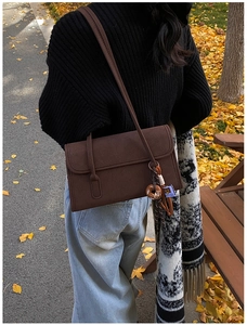 Detail of dark brown vintage matte shoulder bag with donut charm in autumn park setting