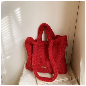 Detail of red plush tote bag with furry texture, handle, and 'our fave' patch on front