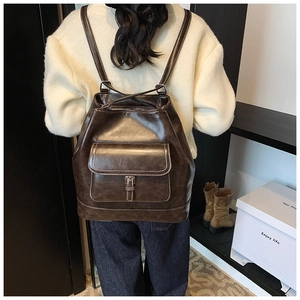 Detail of dark brown PU leather backpack featuring white contrast stitching and buckle