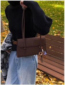 Detail of vintage matte brown shoulder bag with a donut charm in an autumn park setting