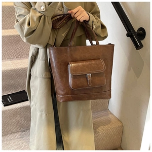 Close-up of retro brown leather tote bag with front pocket flap and metal buckle