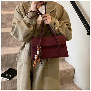 Detail of burgundy matte shoulder bag with stylish charm on a khaki trench coat