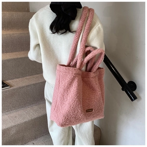 Pink plush teddy tote bag with woven label detail shown in a minimalist lifestyle setting
