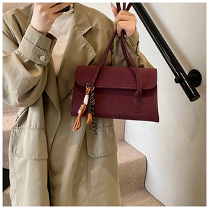 Detail of burgundy matte shoulder bag with vintage tassel charm and slim handles