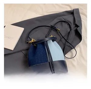 Detail of denim and blue leather bucket bag with gold hardware and drawstring closure