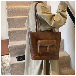 Detail of a dark brown vintage tote bag with front pocket carried by a model in a trench coat