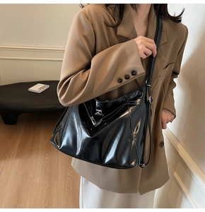 Detail of a large black glossy tote bag with white contrast stitching on a shoulder bag