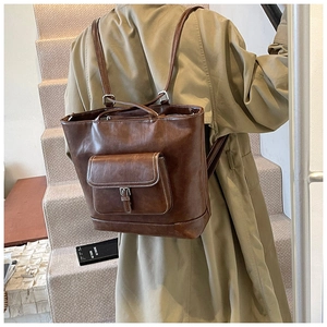 Detailed view of vintage brown leather backpack worn by model in stylish trench coat