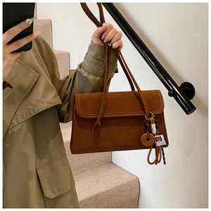 Detail of caramel brown frosted suede shoulder bag with decorative pendant and stitching