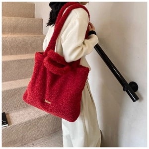 Close-up of red plush tote bag with brand label on a soft faux lamb wool surface