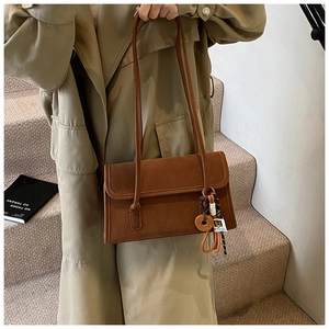 Close-up of a brown suede baguette bag with decorative wooden charm on a beige trench coat